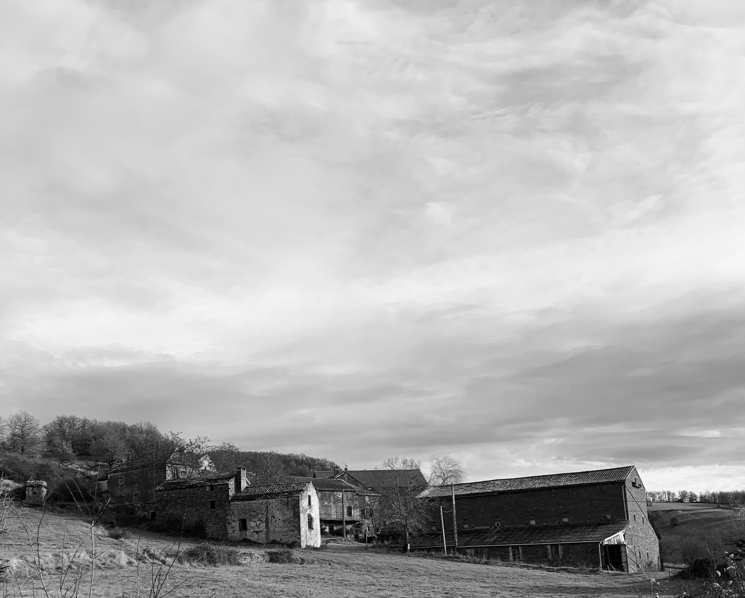 Vue en noir et blanc des bâtiments des Roques au sein du grand paysage agricole de l’Aveyron